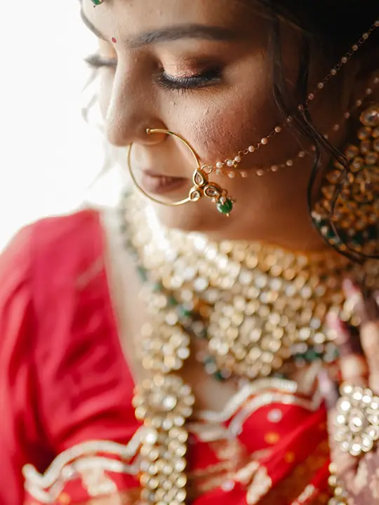 Close portrait of Monika wearing a red sari and traditional bridal jewellery.