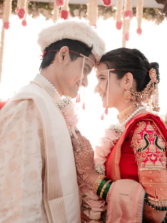 Swaraj and Anuja share a quiet moment in traditional wedding attire beneath floral decorations.