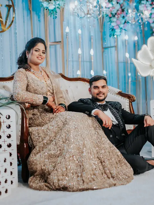 Varsha and Shubham at their reception against a blue and floral backdrop.